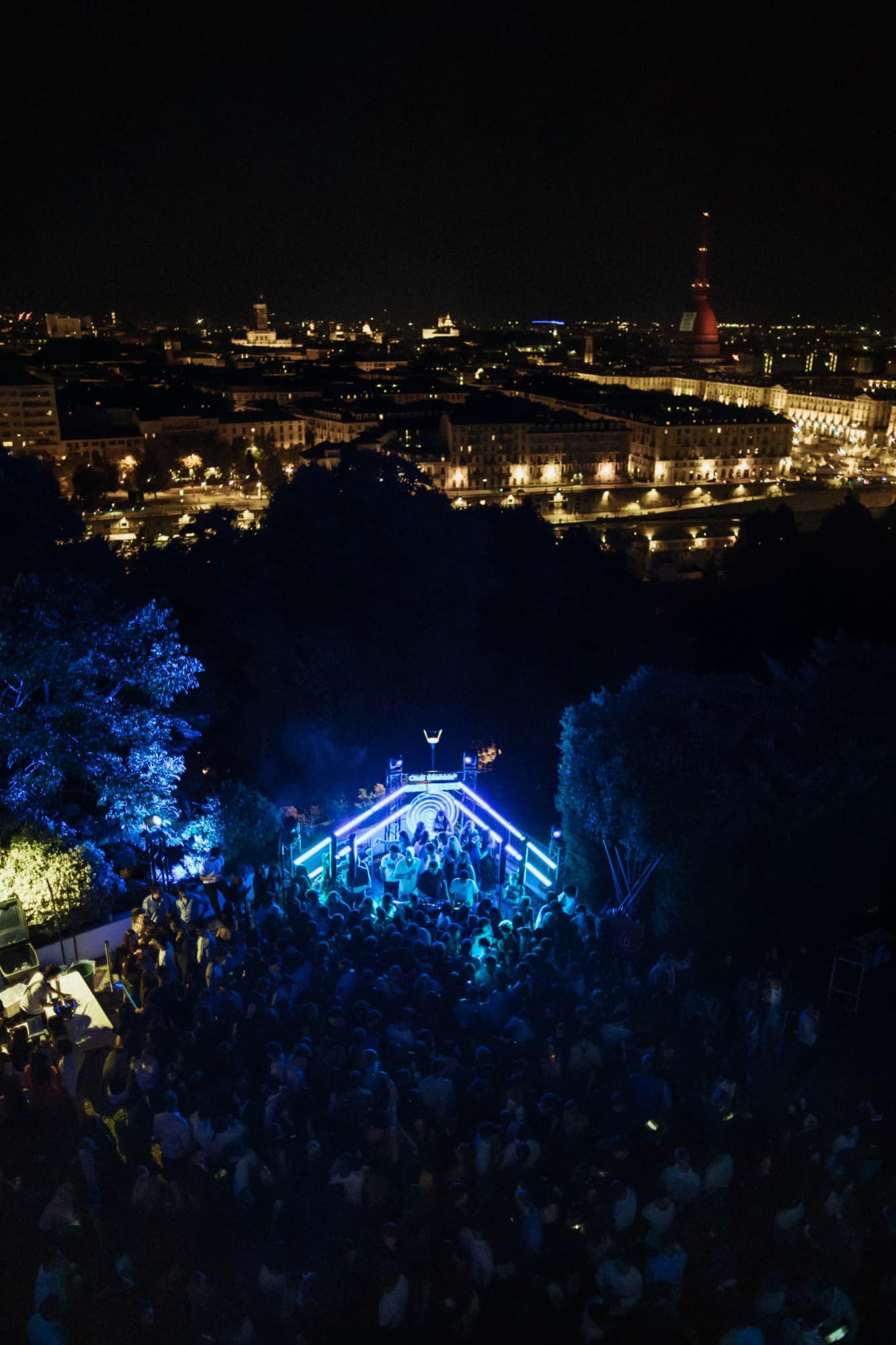 The crowd around the blue-lit DJ booth at Monte dei Cappuccini, Torino and the Mole Antonelliana behind